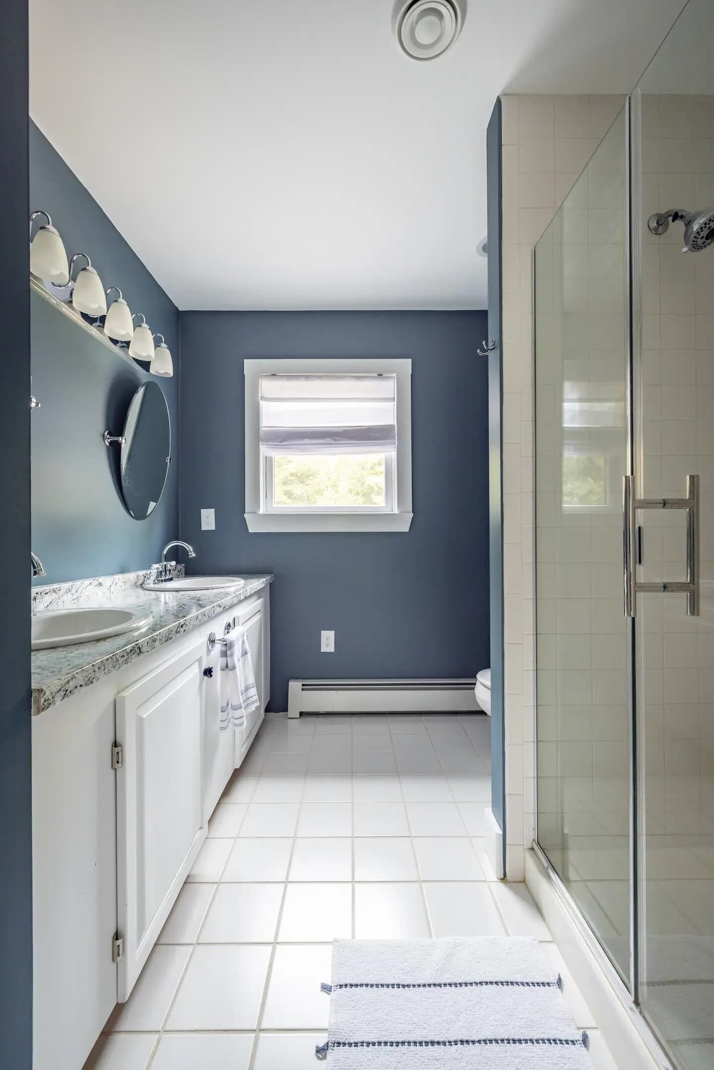 A bathroom with a large window, a shower, and a sink with a mirror.
