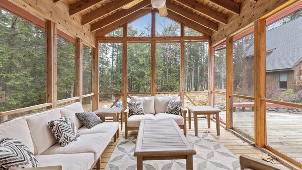 Un espace extérieur aménagé, abrité et doté d’un plafond en bois, de grandes fenêtres et d’une vue sur la forêt.