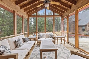 A covered outdoor seating area with a wooden ceiling, large windows, and a view of the forest. - “Big Red” @ New London/Sunapee | Lake-Ski-Wellness (New London)