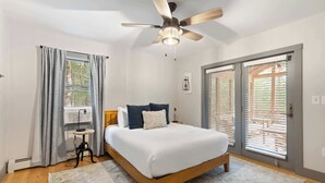 Une chambre à coucher avec un lit, un ventilateur de plafond, une fenêtre avec des rideaux et une porte avec des stores.