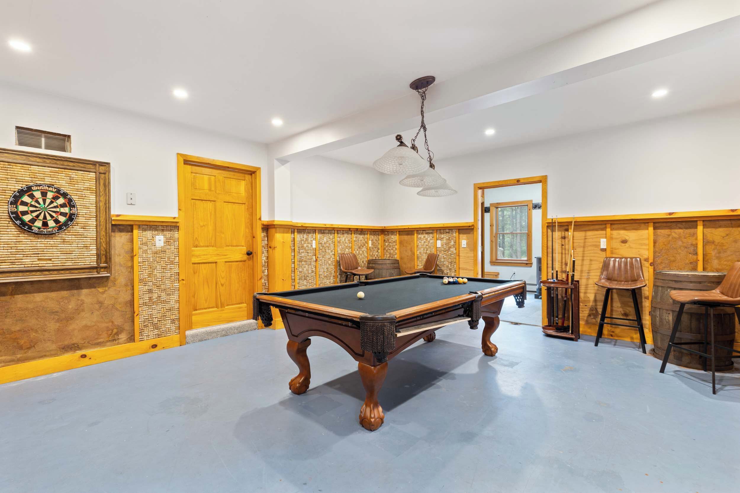 Una mesa de billar en una sala con paneles de madera, un dardo y una lámpara colgante.
