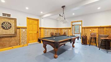 Una mesa de billar en una sala con paneles de madera, un dardo y una lámpara colgante.