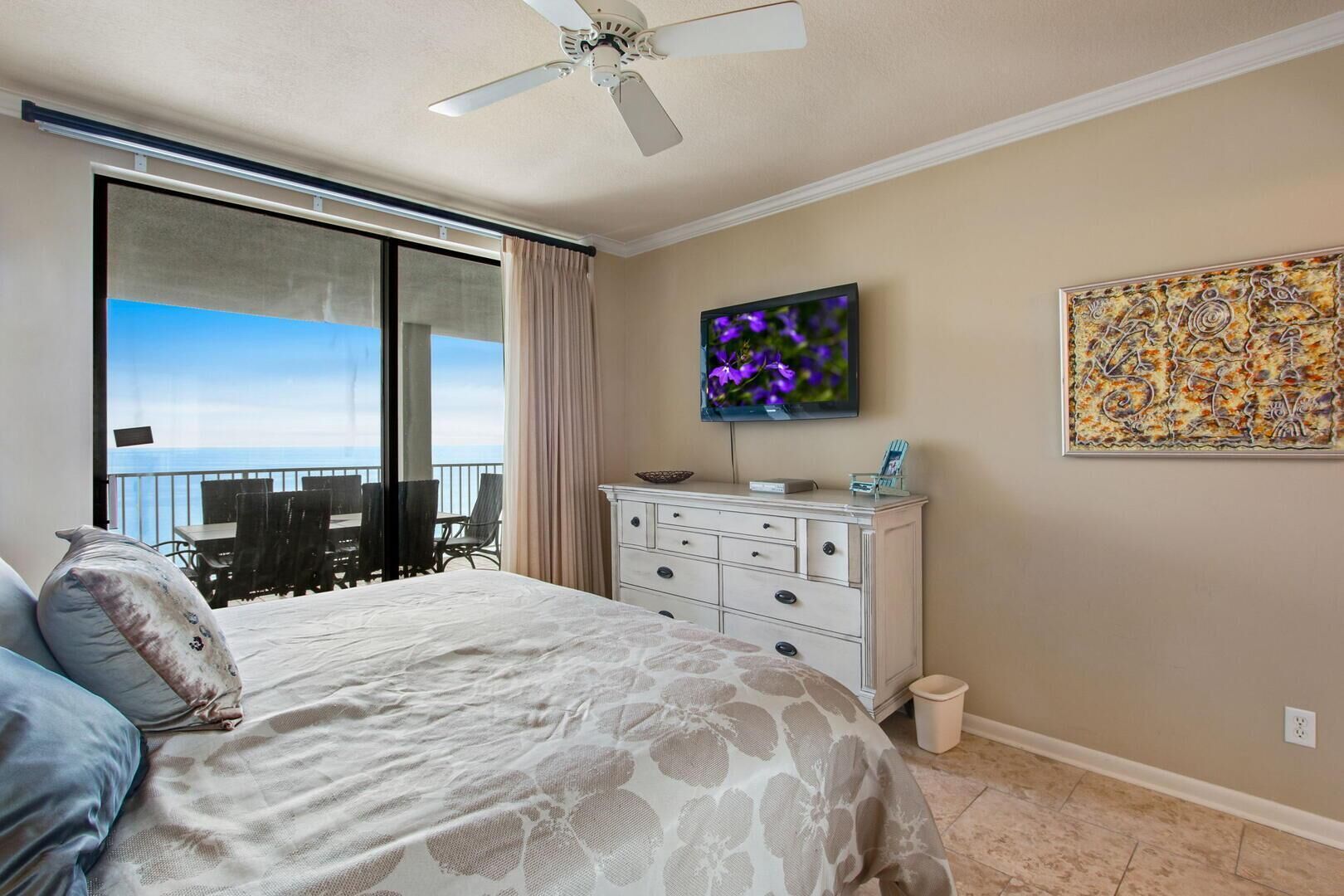 A bedroom with a bed, a dresser, a television, and a large window with a view.