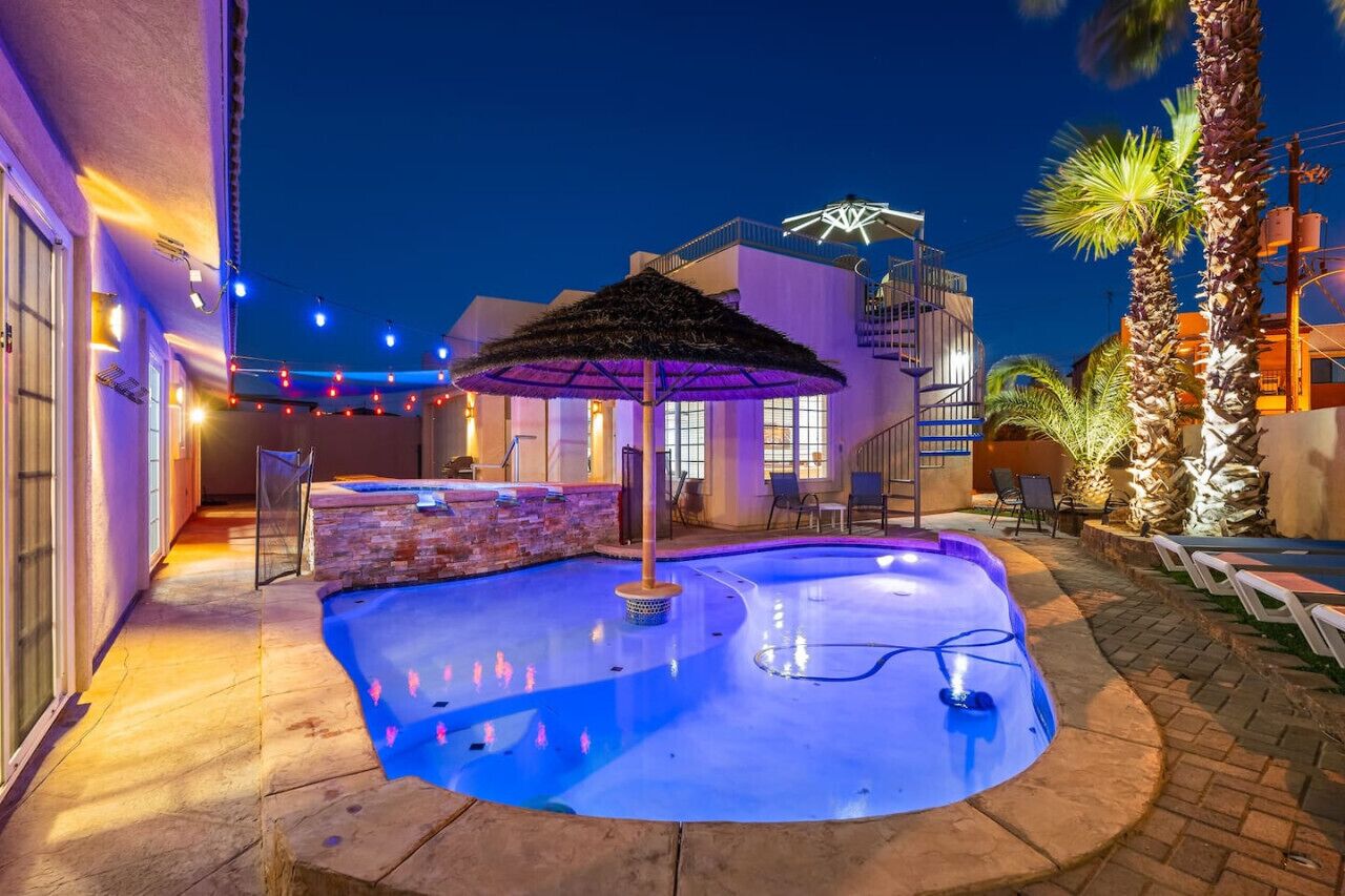 A pool area with a thatched umbrella, lounge chairs, and a palm tree.