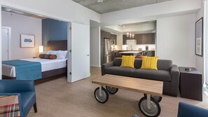 Ein modernes Hotelzimmer mit Bett, einer Couch, einem Esstisch und einer Küchenzeile.