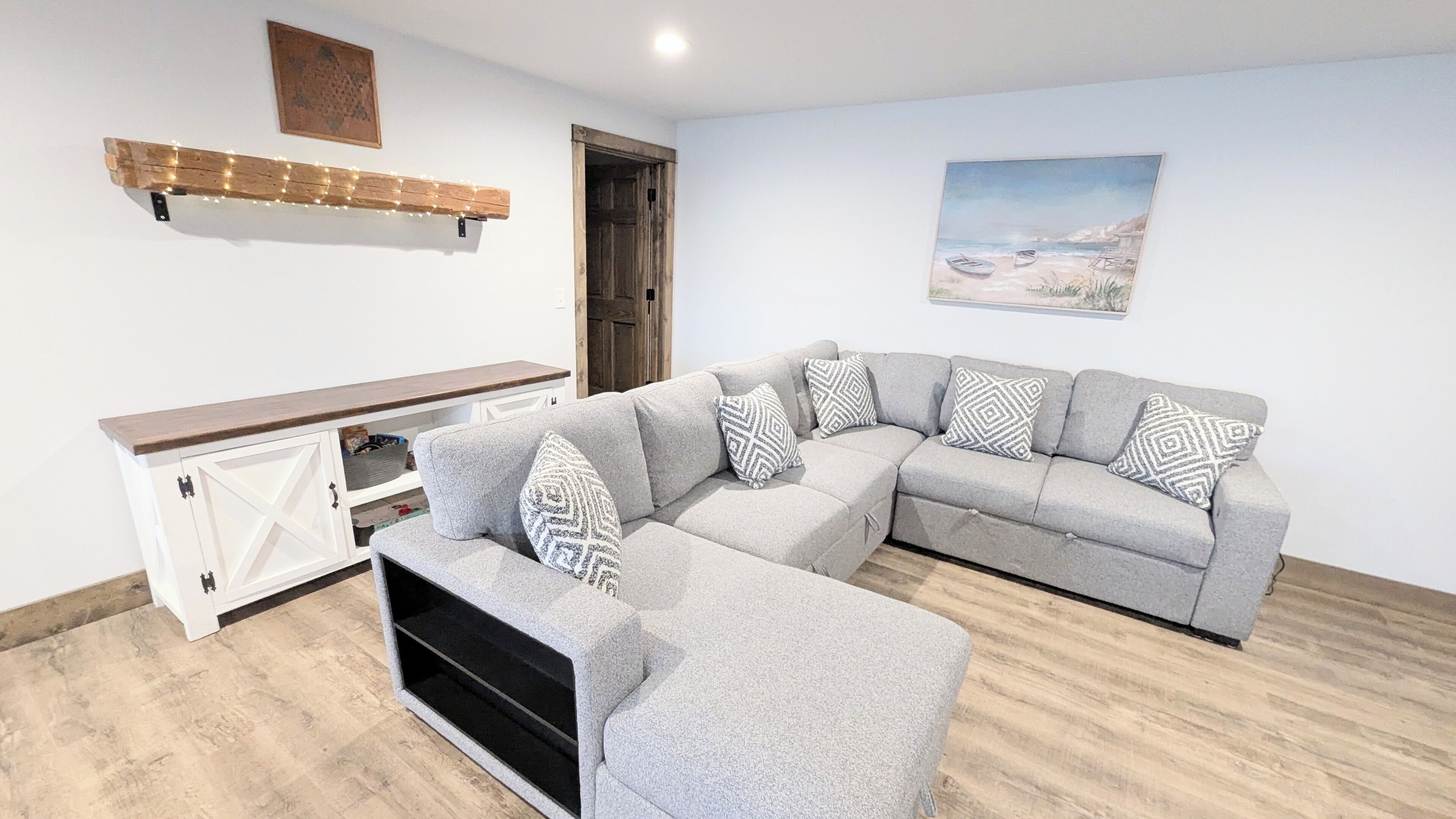 Ein modernes Wohnzimmer mit einem grauen Ecksofa, einem Holztischchen und einem Gemälde mit einer Strandansicht.