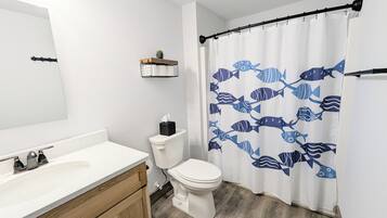 A bathroom with a white toilet, a sink with a wooden cabinet, and a shower curtain with a fish pattern.