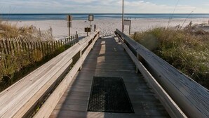 Ein hölzerner Steg führt zu einem Strand mit einer Fahnenmast und einer Flagge.