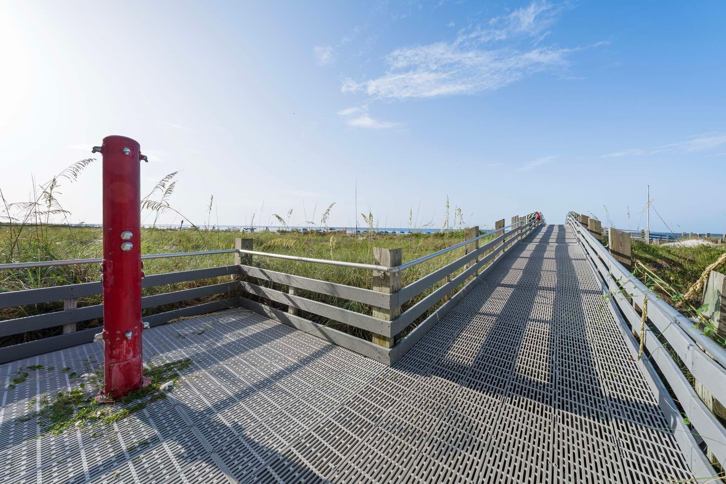 A wooden boardwalk leading to a beach with a red post on the left.