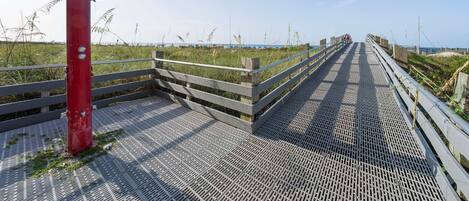 A wooden boardwalk leading to a beach with a red post on the left.