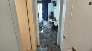 A narrow hallway with a tiled floor leading to a room with a bed and a blue curtain.