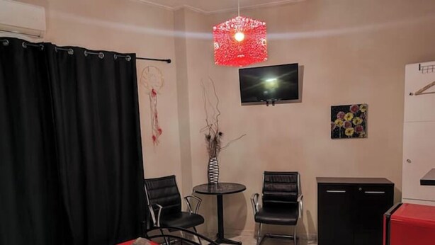 A hotel room with a bed, two chairs, a small table, a TV, and a red refrigerator. - Dream Catcher (Veria)