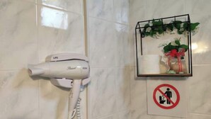 A hair dryer mounted on a tiled wall, a no-smoking sign, and a shelf with a plant and a gift. - Dream Catcher (Veria)