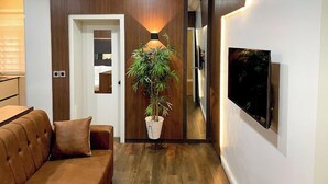 A modern living room with a brown leather sofa, a potted plant, and a flat-screen TV mounted on the wall. - WHTYESCAPE SERVICED APARTMENTS (Abuja)