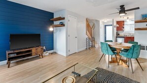 A modern living room with a flat-screen TV, wooden entertainment unit, and a dining area with a wooden table and teal chairs. - Escape to the scenic heights of Hood River (Hood River)