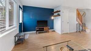 A living room with a blue accent wall, a TV on a wooden stand, a staircase, and a small table. - Escape to the scenic heights of Hood River (Hood River)
