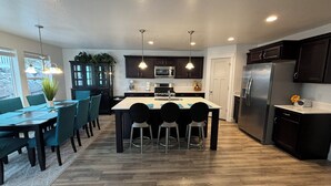 Una cocina moderna con una isla central, armarios oscuros, electrodomésticos de acero inoxidable y una zona de comedor con sillas y una mesa.