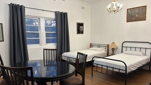 Una habitación con dos camas individuales, una mesa redonda con sillas, un candelabro y una ventana con cortinas.