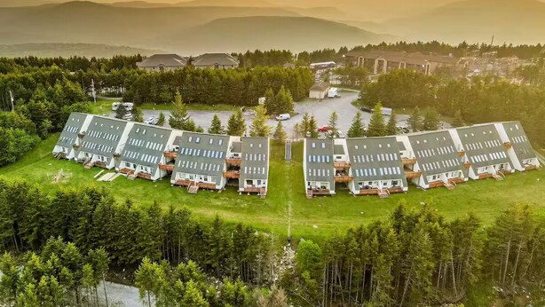 Una hilera de edificios modernos de varios pisos con un patio central, rodeados por un bosque denso.