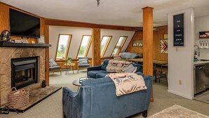 Una sala de estar acogedora con chimenea, un sofá azul y un comedor con cocina al fondo.