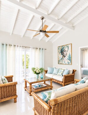 A spacious living room with a ceiling fan, wicker furniture, and a large window with curtains. - Beija Flor Entire home in Oranjestad, Aruba (Opal)