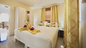 A hotel room with a bed, a bedside table, a window with curtains, and a door leading to another room. - Beija Flor Entire home in Oranjestad, Aruba (Opal)