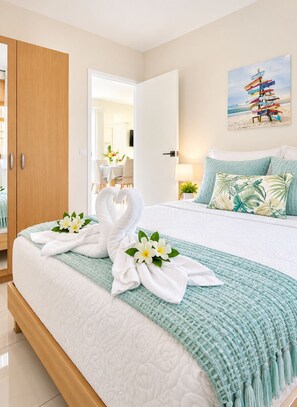 A hotel room with a bed, a painting of a beach, and a door leading to a dining area. - Beija Flor Entire home in Oranjestad, Aruba (Opal)
