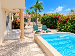 A pool area with a clear blue pool, surrounded by a pebble walkway, and two green lounge chairs. - Beija Flor Entire home in Oranjestad, Aruba (Opal)