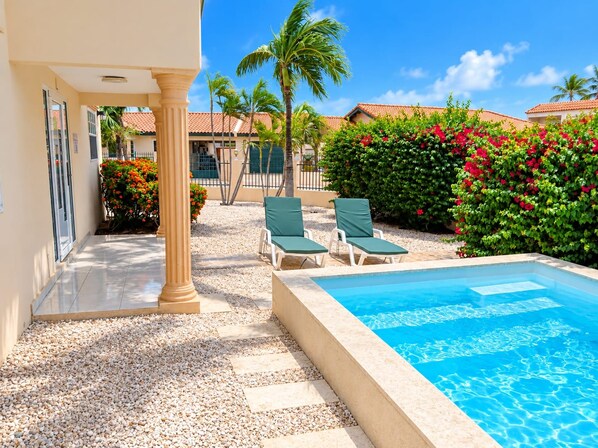 A pool area with a clear blue pool, surrounded by a pebble walkway, and two green lounge chairs. - Beija Flor Entire home in Oranjestad, Aruba (Opal)