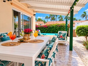 An outdoor patio with a dining table, chairs, and a pool in the background. - Beija Flor Entire home in Oranjestad, Aruba (Opal)