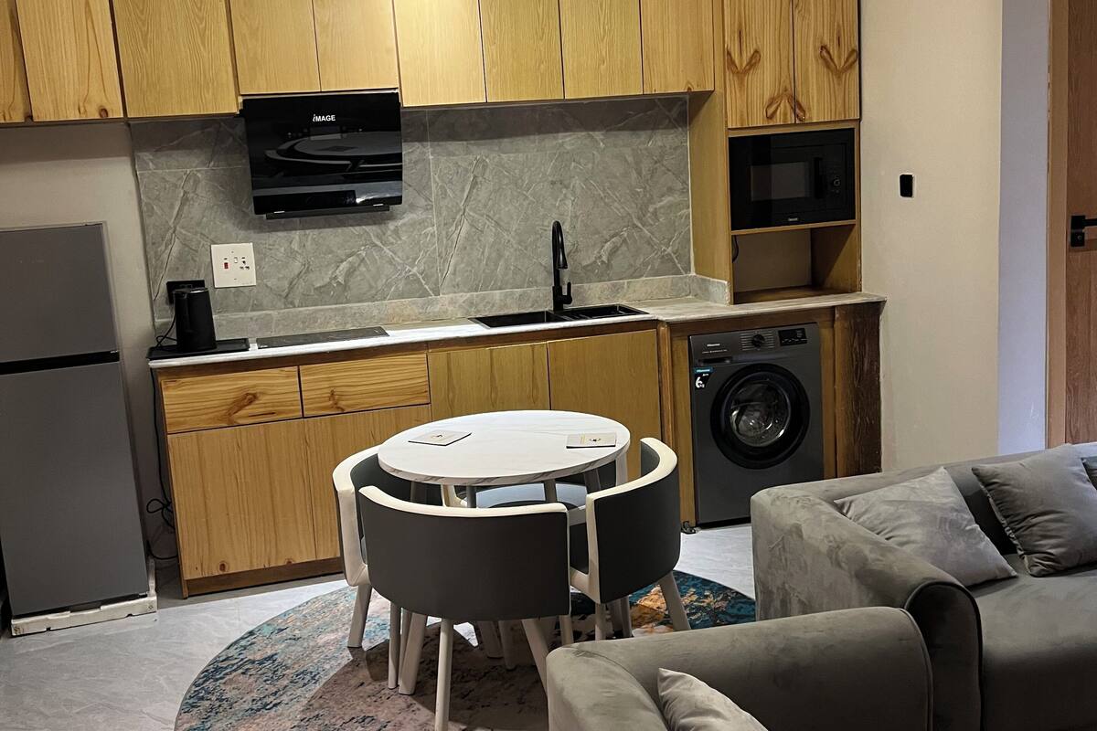 Una cocina compacta con armarios de madera, un microondas integrado y una mesa redonda con sillas.
