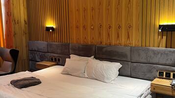 A modern hotel room with a large bed, wooden panel walls, a headboard, bedside tables, and a wall-mounted air conditioner.