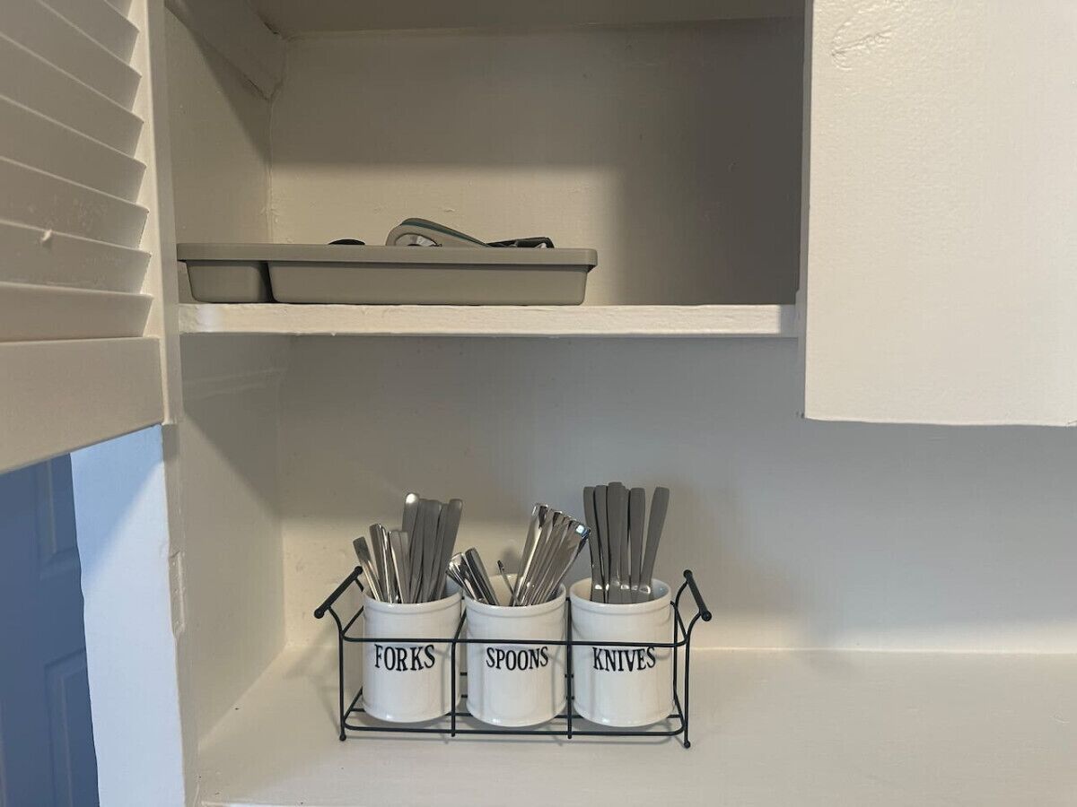 A kitchen with a white cabinet and a metal utensil holder with labeled compartments for forks, spoons, and knives.