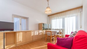 Een moderne woonkamer met een rode bank, houten vloeren, een tv op een houten kast, en een eethoek met een tafel en stoelen.