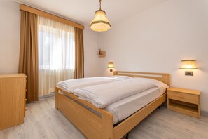 Une chambre à coucher avec un lit en bois, une table de chevet, une commode, une lampe et une fenêtre avec des rideaux.