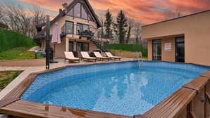 A modern house with a swimming pool, lounge chairs, and a staircase leading to a balcony.