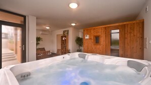 A spa room with a large hot tub, wooden walls, and a small seating area with chairs and a table.