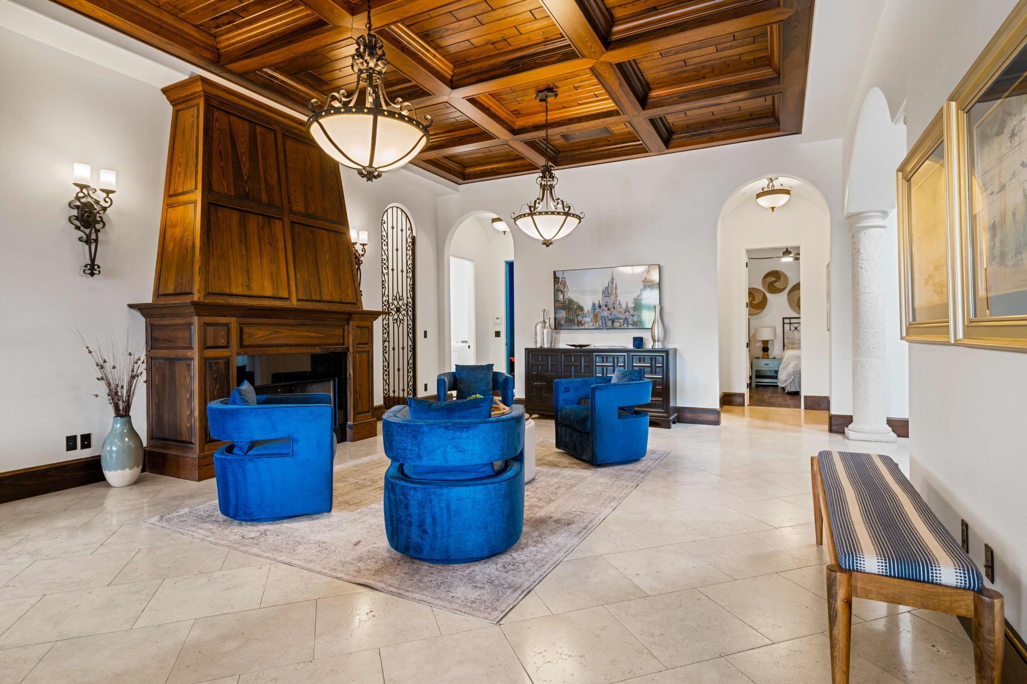 A spacious lobby with a high ceiling, wooden paneling, and a large fireplace. There are blue upholstered seating areas and a bench along the wall.