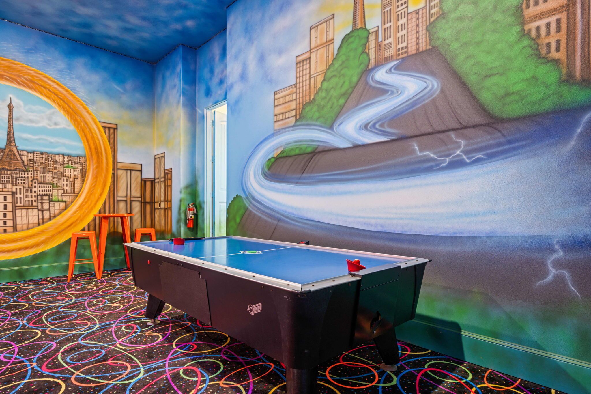 A room with a pool table, colorful floor patterns, and a mural depicting a cityscape with a river and lightning.