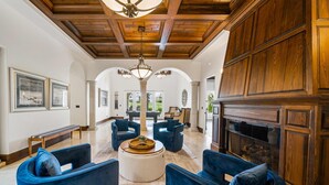 A spacious living room with a high ceiling, wooden paneling, and a fireplace. There are several blue armchairs and a round ottoman. - 5BR Luxury Villa • Games & Golf • Near Disney (Reunion)