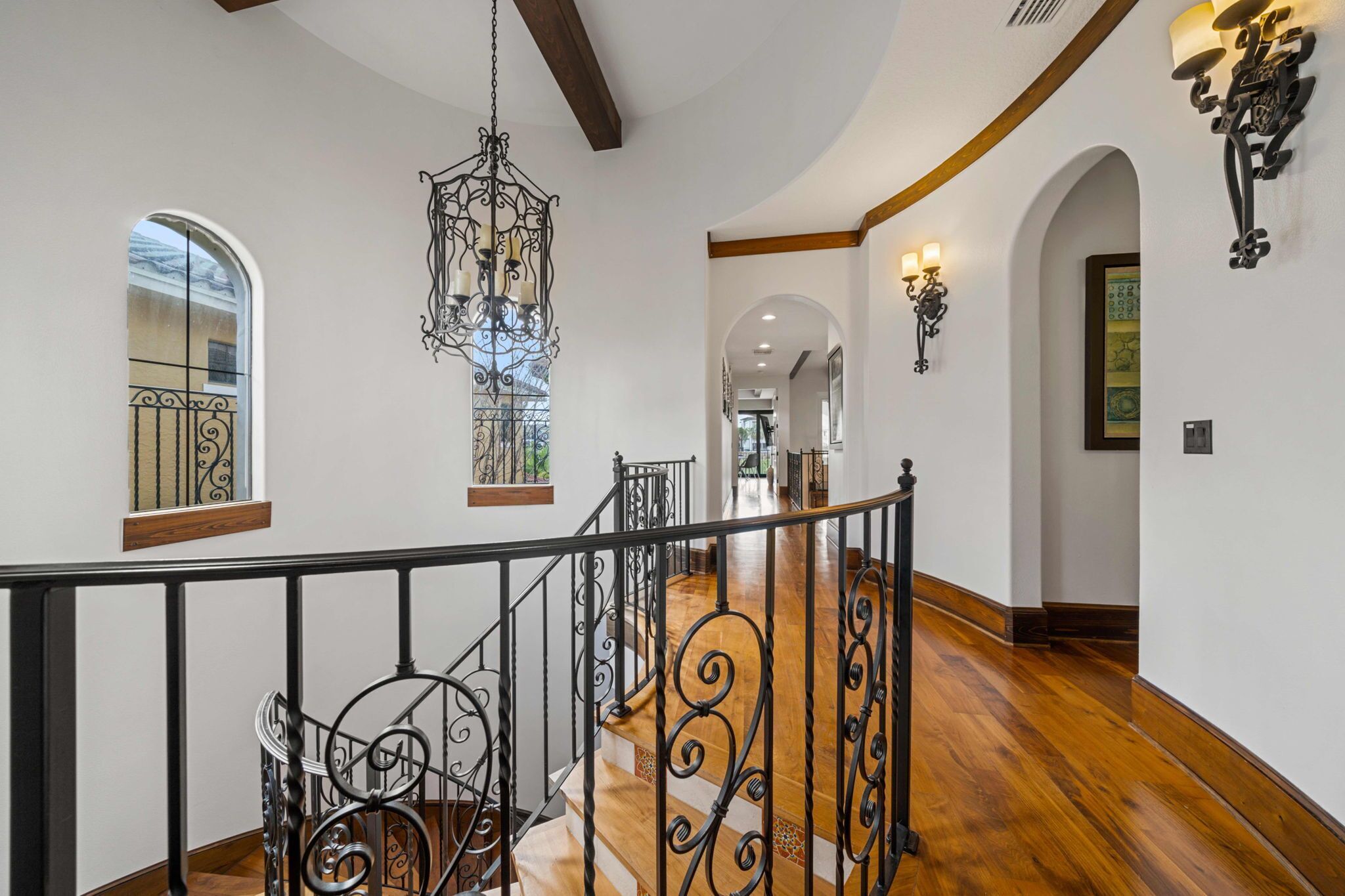 A spacious interior with a wooden staircase, ornate black railings, and a chandelier.