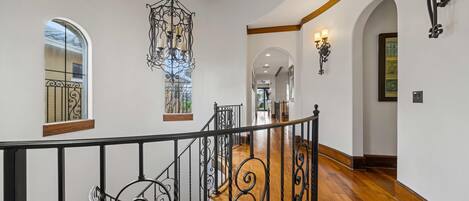 A spacious interior with a wooden staircase, ornate black railings, and a chandelier.