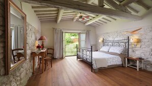 A bedroom with a stone wall, a bed with a metal frame, a wooden floor, a table with chairs, and a window with curtains. - Casa al Fiume - Villa with private pool (Terranuova Bracciolini)