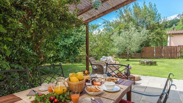 An outdoor dining area with a table set for breakfast, surrounded by greenery and a wooden fence. - Casa al Fiume - Villa with private pool (Terranuova Bracciolini)