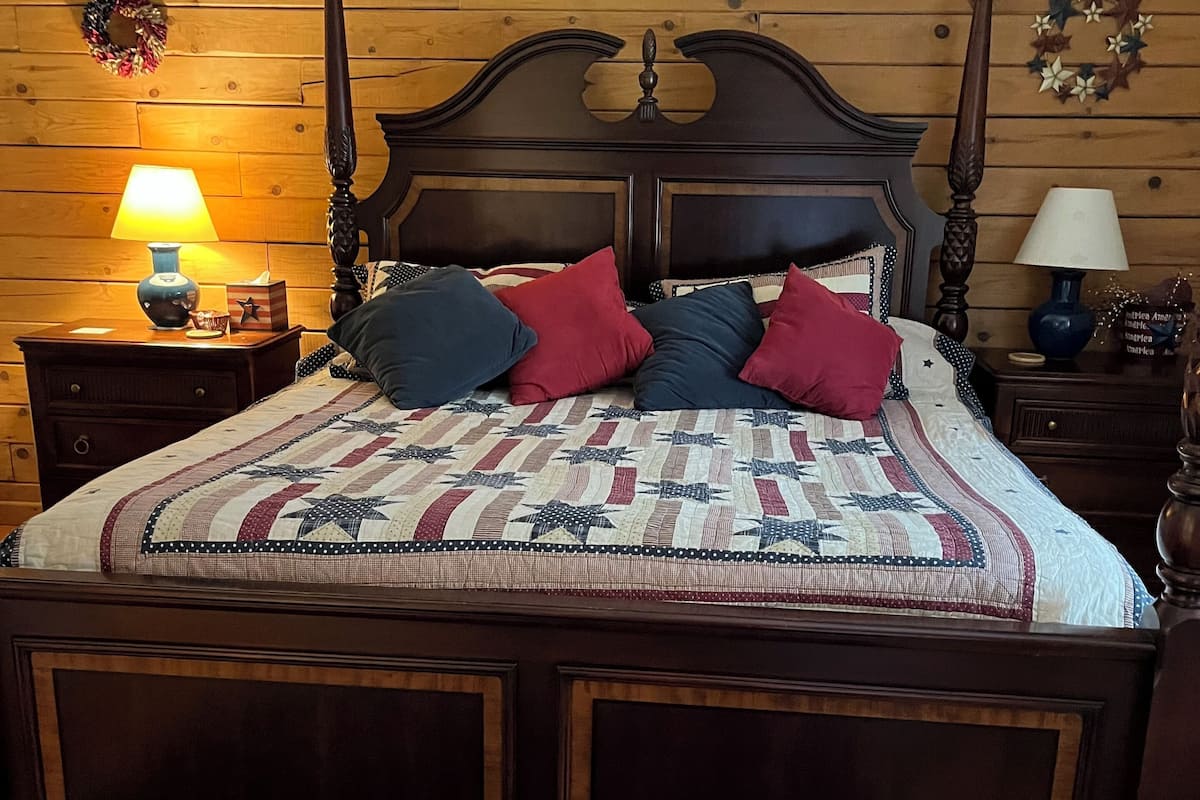 A wooden-paneled bedroom with a large bed, two bedside tables, and a blue rug.