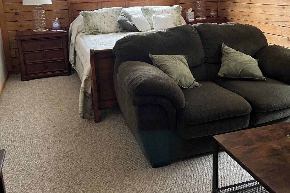 A cozy room with a bed, a sofa, a small table, and a ceiling fan.
