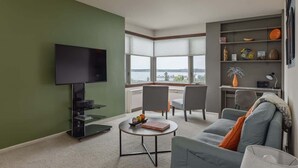 A modern living room with a flat-screen TV, a sofa, a coffee table, and a bookshelf. - Artsy 1 Bedroom Condo with the Views to the Inlet! (Anchorage)