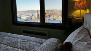 A bedroom with a large window offering a view of a snowy landscape and buildings. - Artsy 1 Bedroom Condo with the Views to the Inlet! (Anchorage)