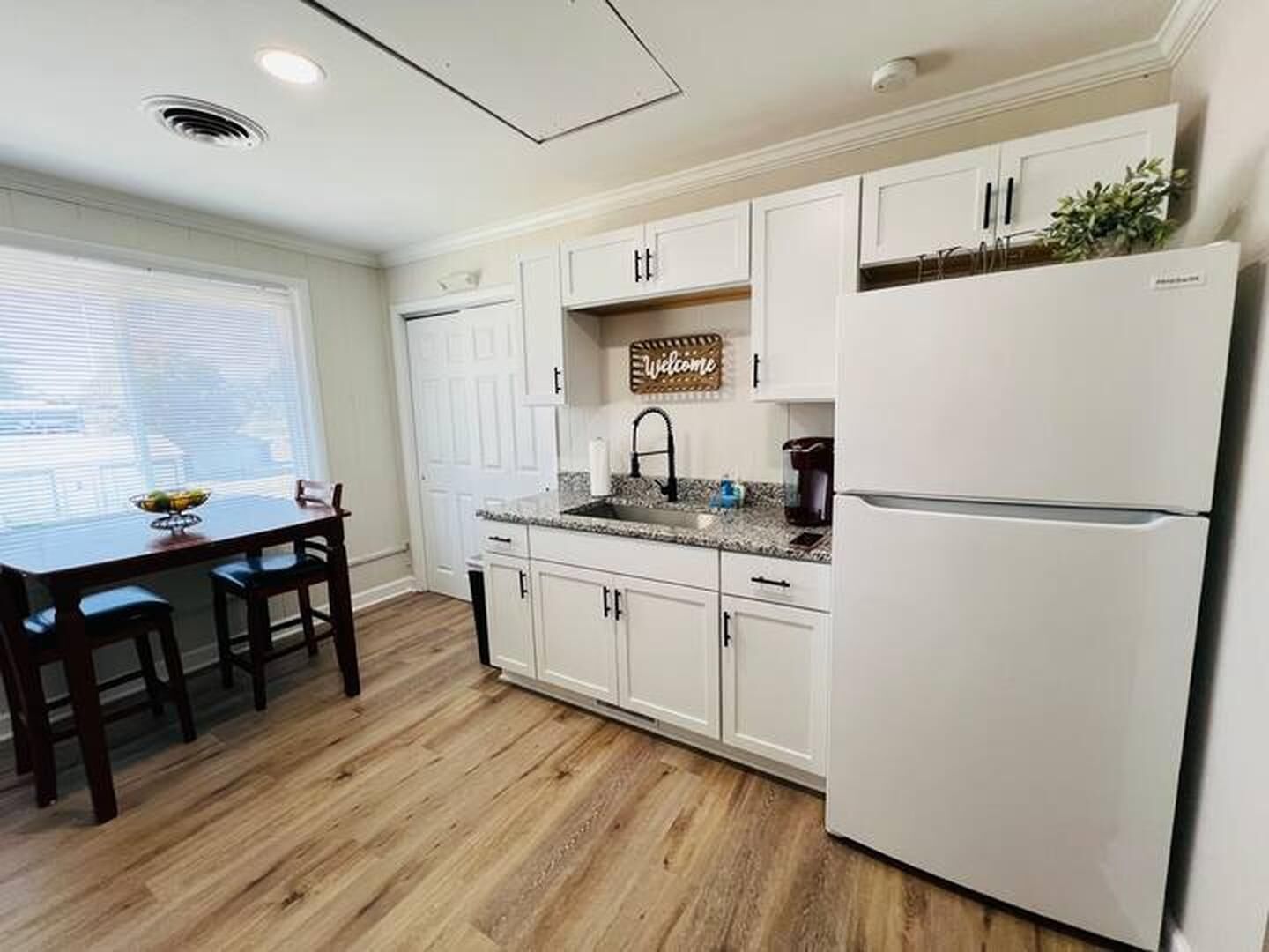 A kitchen with white cabinets, a white refrigerator, a sink, and a welcome sign.