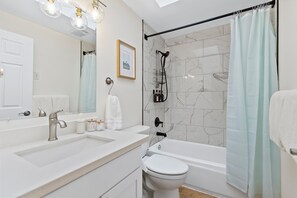 A modern bathroom with a white sink, a toilet, a bathtub, and a shower with a glass door. - Modern 3BD house in walkable Ballard, family and dog-friendly, A/C, fenced yard (Seattle)